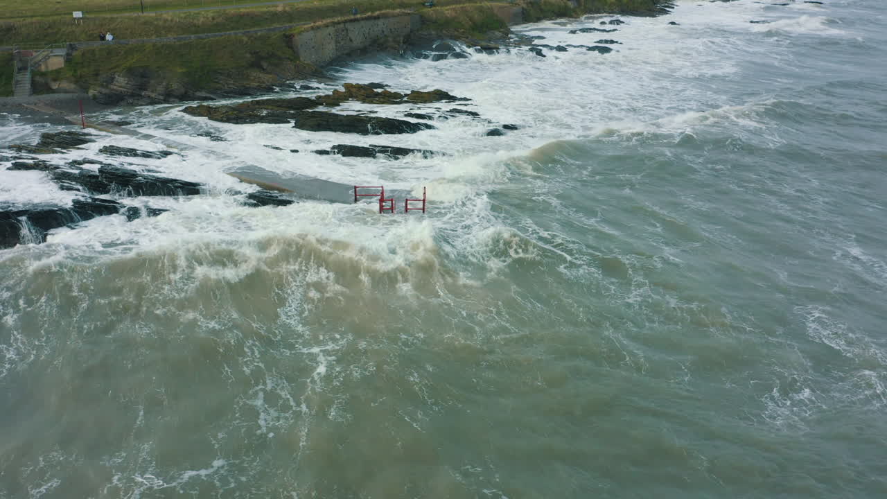 vista aérea de las olas rompiendo contra las rocas a lo largo de la costa durante una tormenta
