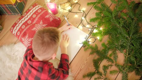 Young-boy-is-laying-on-the-floor-and-writing-his-wishlist-for-Christmas