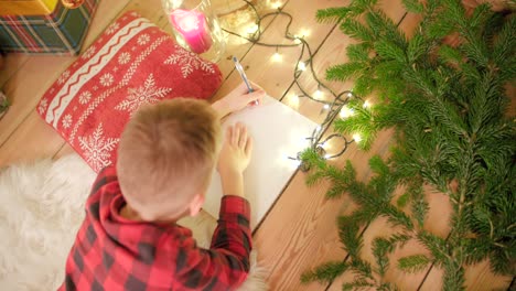 el niño está tirado en el suelo y escribiendo su lista de deseos para navidad