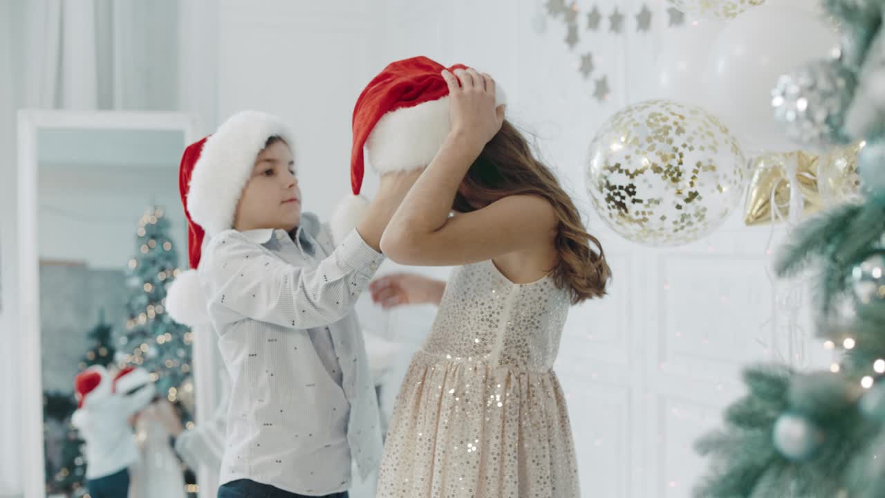niño serio con sombrero de santa sobre niña en apartamento de año nuevo.