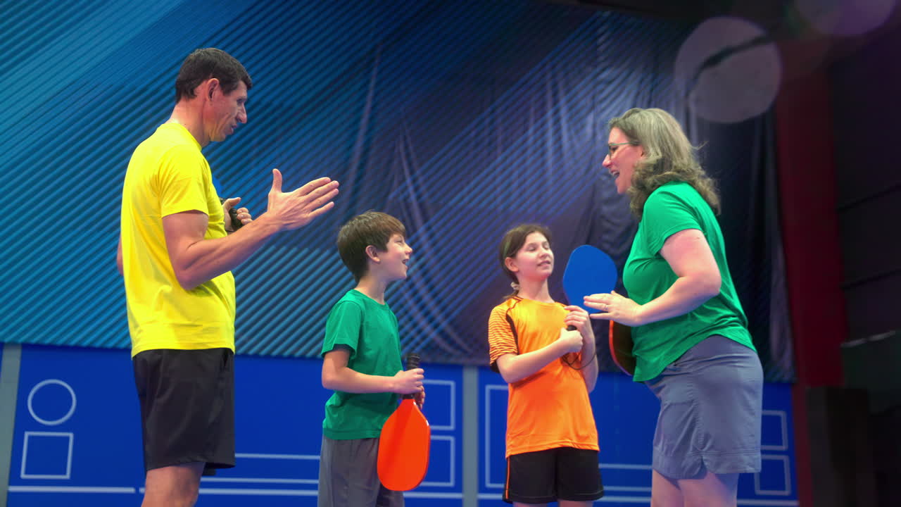 Two adults and two children high-fiving after playing pickleball on a blue, inside court