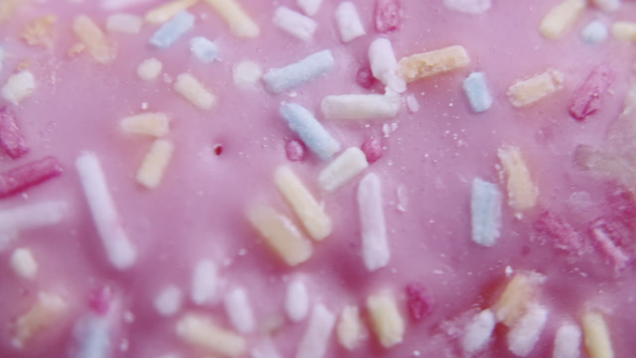 Macro top shot of a pink donut spinning clockwise. A lot of details visible. Colorful sprinkles on the icing.