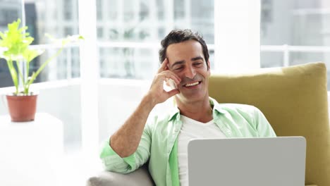 hombre sonriente sentado en el sofá y usando computadora portátil en la sala de estar