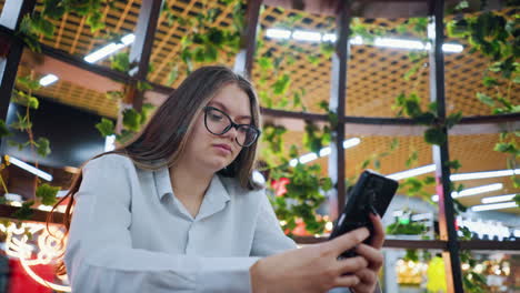 mujer de negocios sentada en un sentado de madera decorativo, hablando con el cliente por teléfono con una sonrisa sutil, en un restaurante bien decorado en un centro comercial bullicioso, mostrando un ambiente profesional