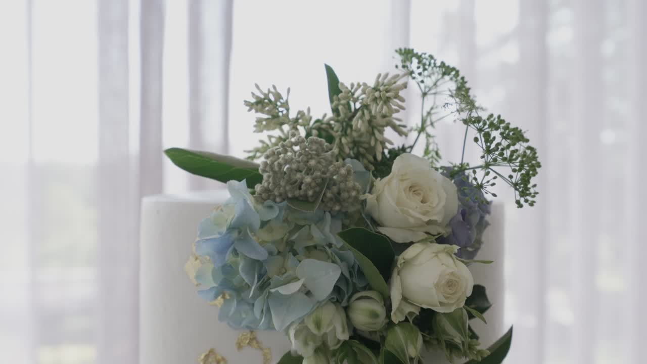Close up of delicate white and blue flowers arranged on a wedding cake with greenery