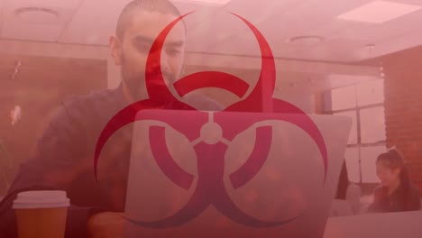 animation of biohazard symbol over biracial businessman using laptop in office