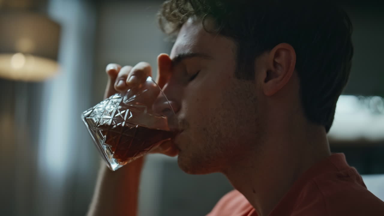Lonely alcoholic sipping bourbon at home closeup. Hopeless man drinking alcohol