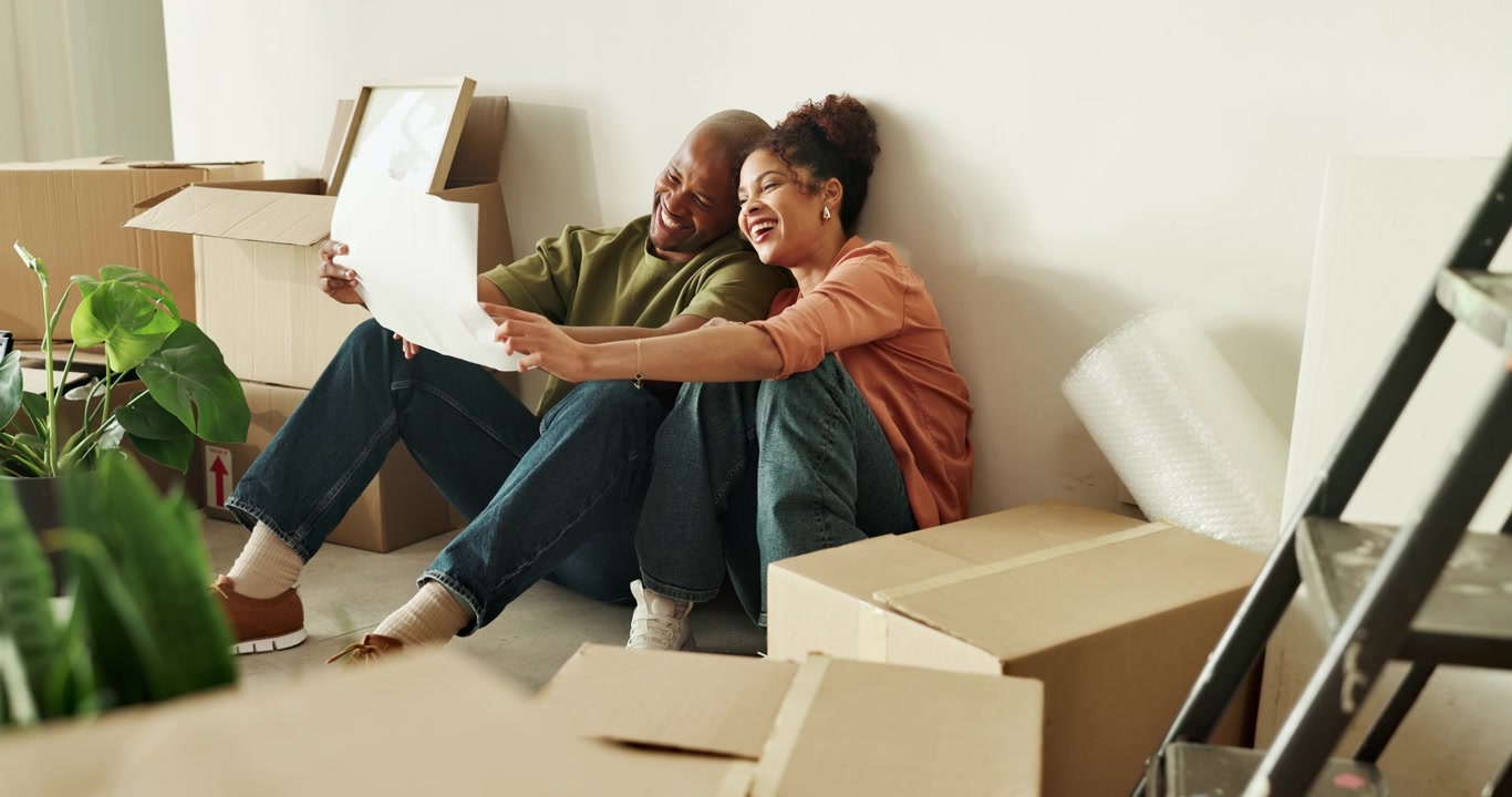 Happy Couple Sitting on Floor Looking at Floor Plan in New Home