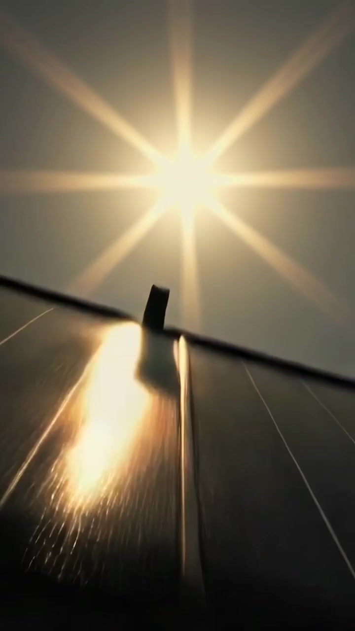 Vertical video: Panning camera up roof solar panels as sun glint creating seam glare and lens flare