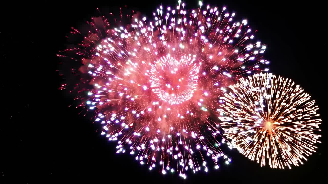 Aerial view of heart-shaped fireworks exploding against a dark sky, captured in a vibrant