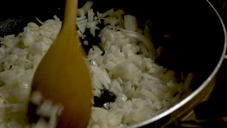 close up view of wooden spoon stirring diced onions in frying pan