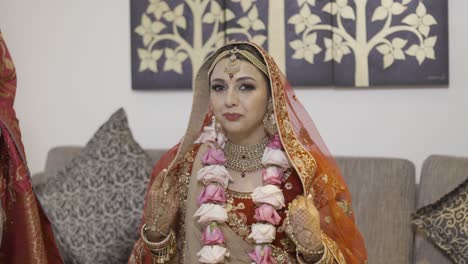 une mariée indienne en tenue de mariée assise dans le canapé et souriant à la caméra avant son mariage