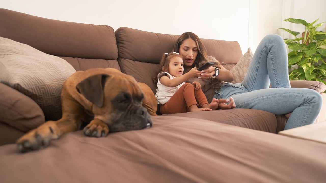 Boxer dog resting by mother and girl watching TV at home