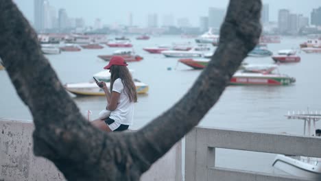 girl in cap white shirt and black shorts sits against sea