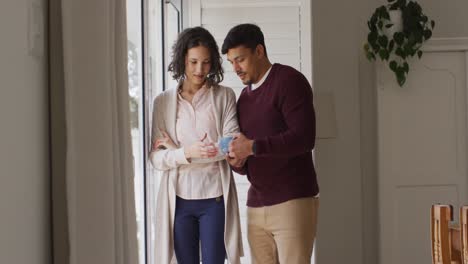 una feliz pareja hispana de pie en la ventana abrazándose tomando café