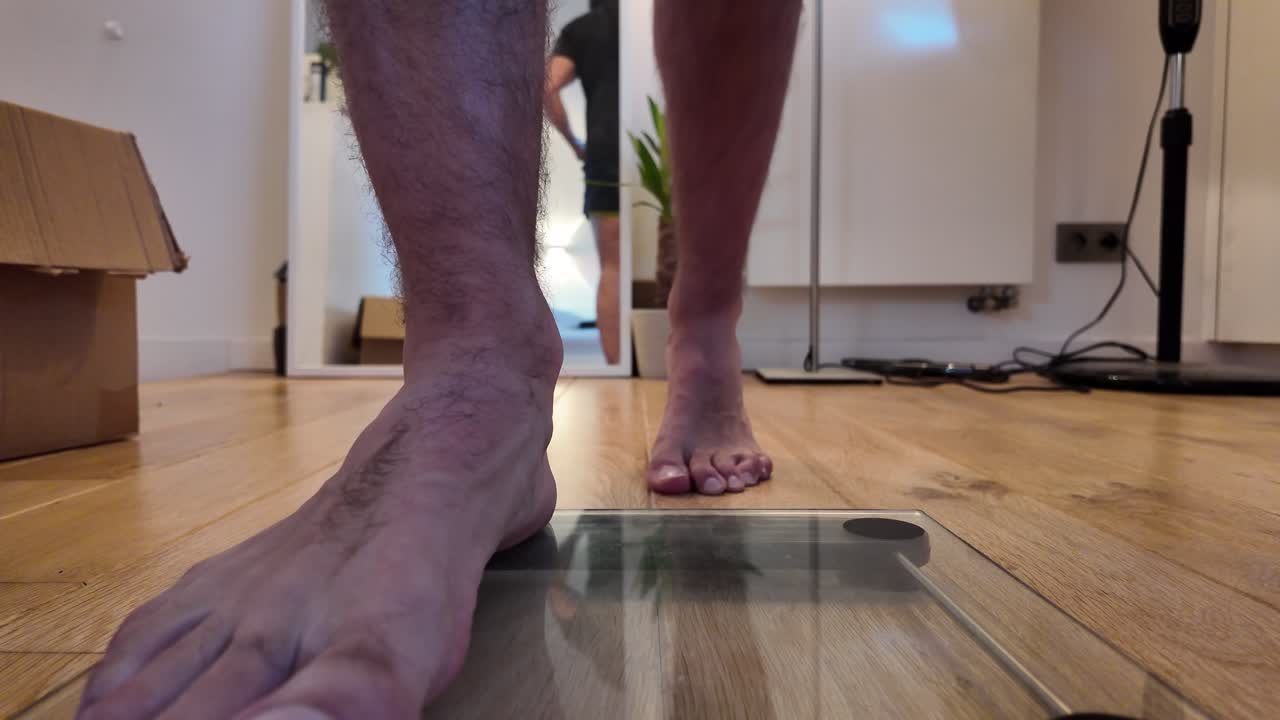 Foot approaches glass scale on wooden floor