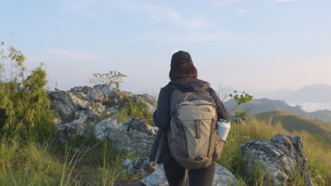 Mittelaufnahme-Einer-Jungen-Rucksacktouristin,-Die-Entlang-Hoher-Gräser-Auf-Dem-Gipfel-Des-Berges-Spazieren-Geht