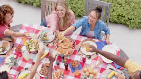 Fröhliche,-Vielfältige-Gruppe-Von-Freunden,-Die-Am-Esstisch-Im-Garten-Anstoßen,-Zeitlupe