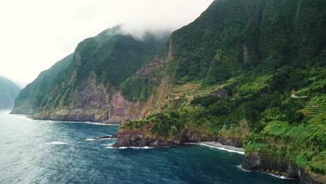 aerial view of the rugged coastline meeting the lush green cliffs, creating a breathtaking contrast between the deep blue ocean and vibrant vegetation in seixal, north of madeira island, portugal