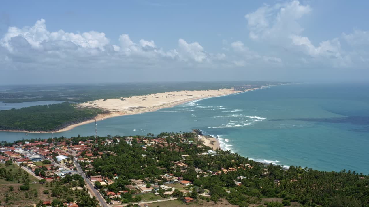Rotating aerial drone extreme wide shot of the tropical beach town of Tibau do Sul in Rio Grande do Norte, Brazil with the Malemb&aacute; Sand Dunes, Atlantic Ocean, and Guara&iacute;ras Lagoon in the background