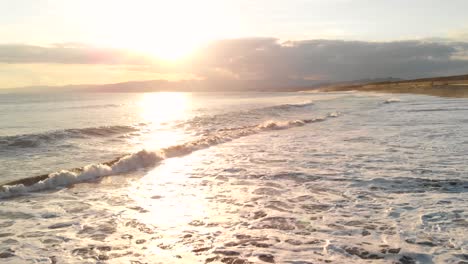 pov cerrar una antena en aumento sobre las olas rompiendo en la playa durante la puesta de sol