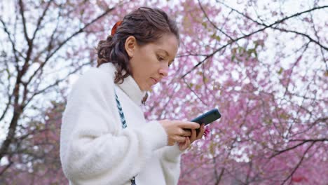 woman using phone amidst cherry blossoms
