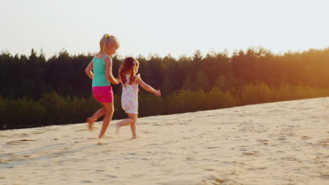 Zwei-Fröhliche-Mädchen,-Die-Bei-Sonnenuntergang-Ein-Rennen-Auf-Dem-Sand-Laufen-Lassen-Kinderspiele-Eine-Glückliche-Kindheit-Prores-Hq