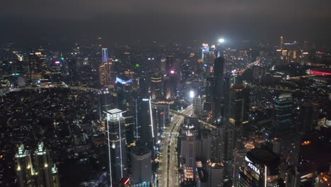 Retreating-dolly-aerial-wide-shot-of-busy-multi-lane-road-intersection-in-modern-urban-city-center-of-Jakarta