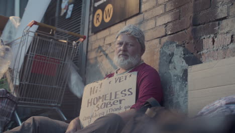 portrait of senior homeless man holding cardboard sign with plea on street