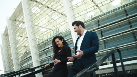 Side-view-business-man-and-woman-smiling-outside.-Couple-walking-downstairs