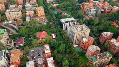 high drone shot pulling back and rotating over bogotá city, revealing trees, buildings, streets, and a tennis court.