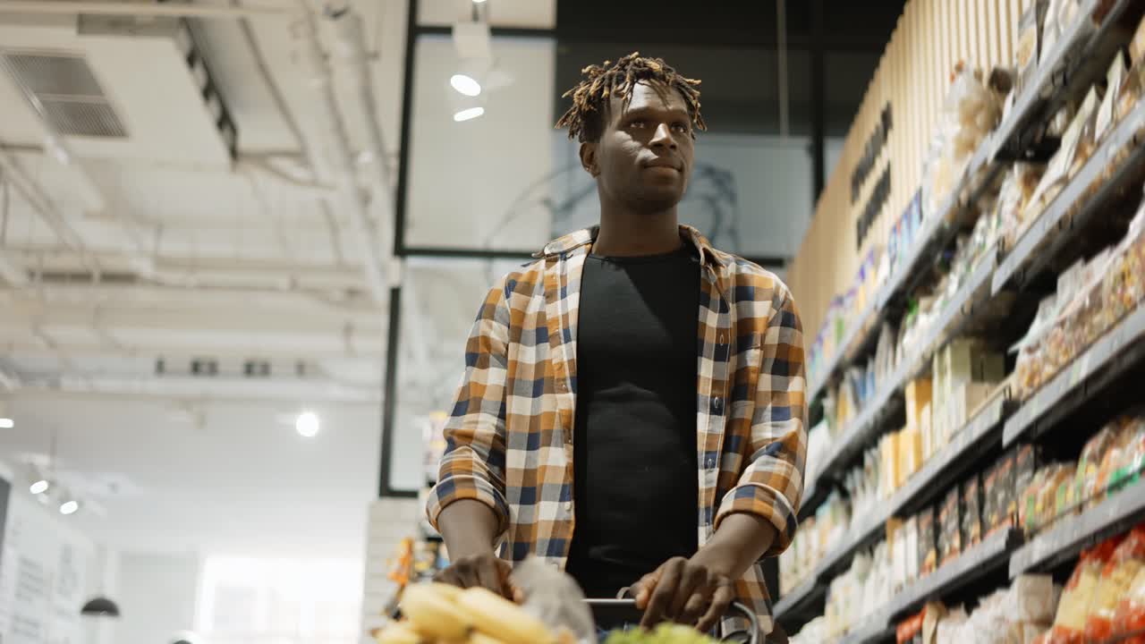 Uomo che spinge il carrello lungo la corsia di un supermercato, vista dal basso