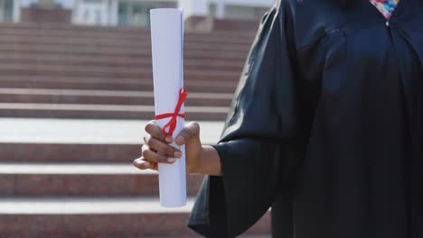 diploma of higher education vertically in the hands of an african-american female university graduate on the background of the stairs from the outside.