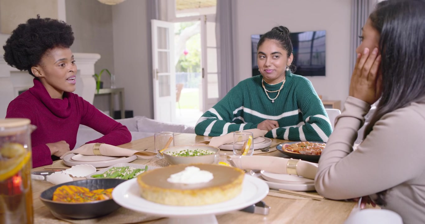 Amigas Diversas Conversando y Riendo en la Mesa, con un Plato Caliente Cerca de un Soporte para Pastel para la Cena