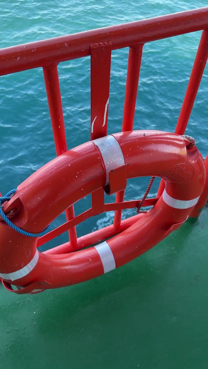Red Lifebuoy Hanging on a Boat Railing with Blue Ocean Water