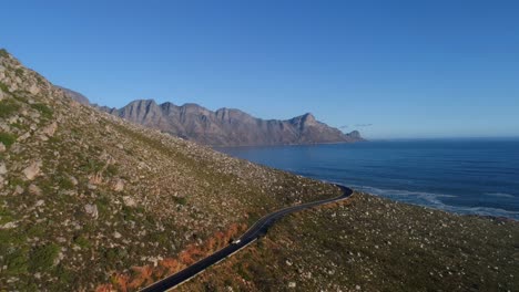 Aerial-drone-view-of-Land-rover-car-driving-along-a-bendy-mountain-pass-road-with-view-of-the-ocean-on-a-clear-sunny-summer-day