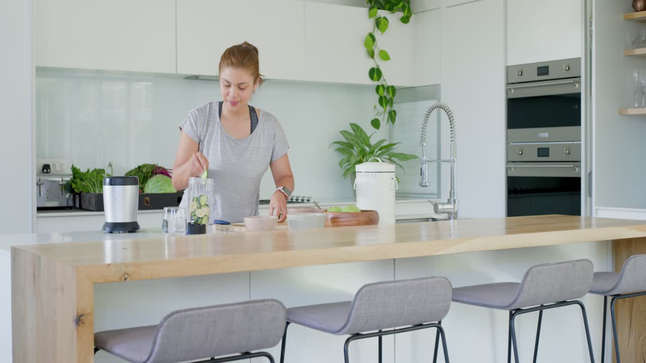 Donna adulta che controlla i prodotti sull'isola della cucina, tritando e aggiungendo verdure al frullatore per un pasto