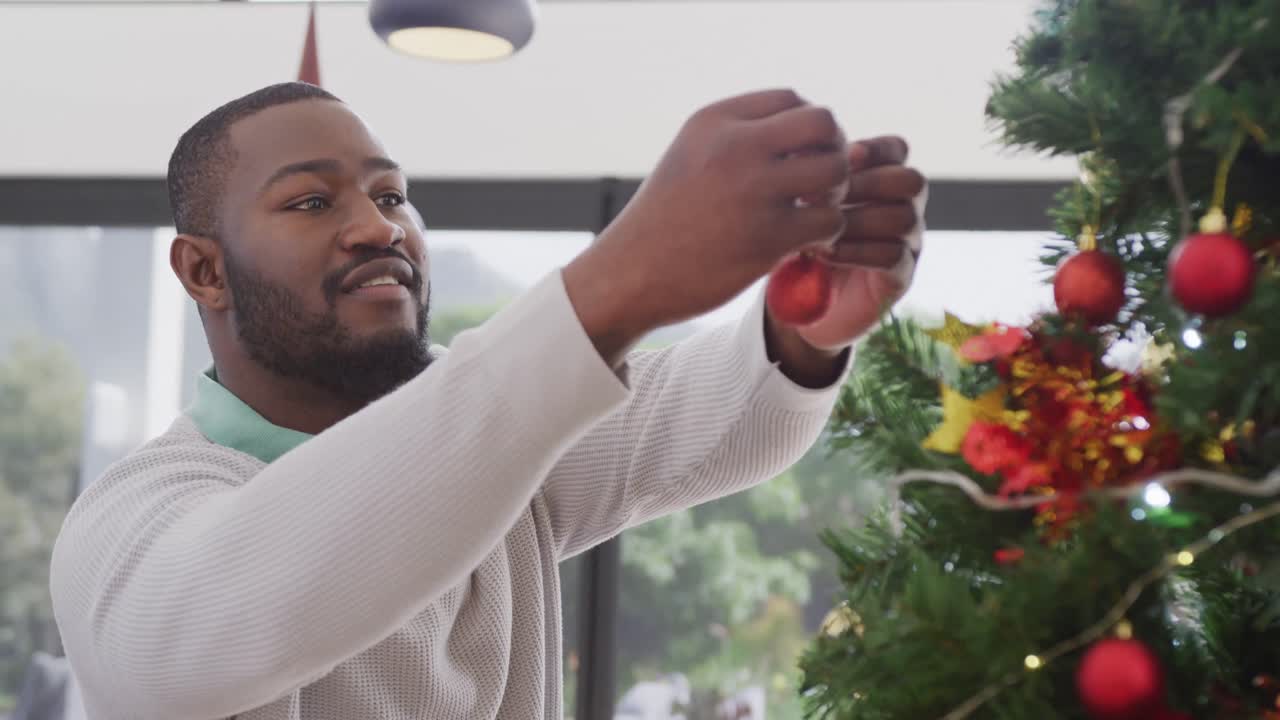 video de un feliz hombre afroamericano decorando un árbol de navidad en casa