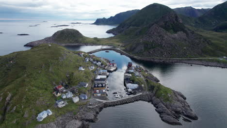 Aerial-forward-view-of-small-fishing-village-nestled-into-a-small-sheltered-cove-along-the-mountainous-coast-of-northern-Norway-on-a-summer-day