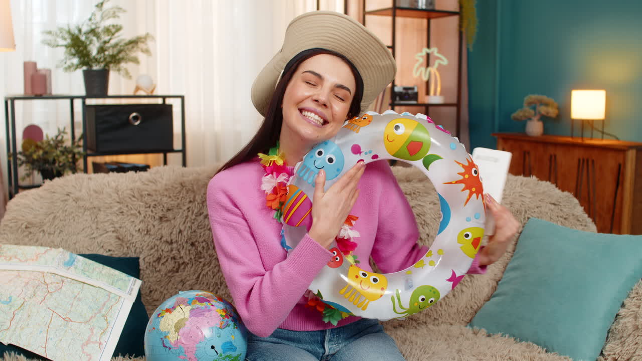 Happy woman on sofa with swim ring holding globe and plane tickets planning exciting future trip