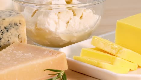 a variety of cheeses and butter arranged with rosemary garnish on a wooden table.