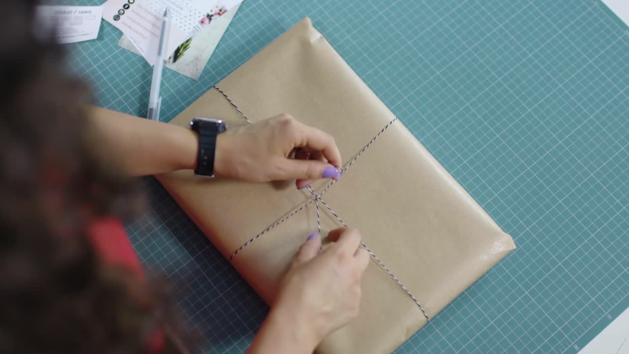 female wrapping present with gray paper with string at the table