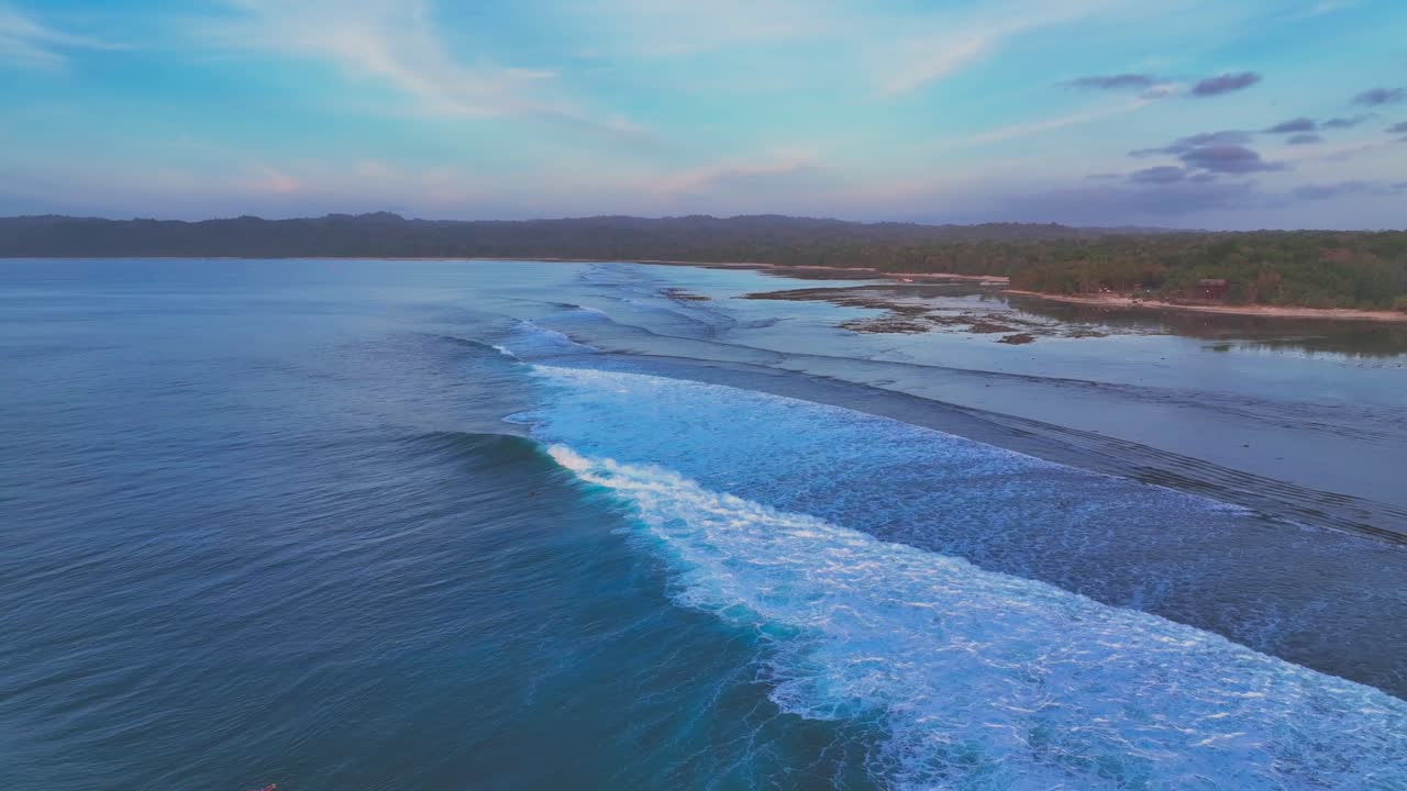 바다의 파도와 산호초의 드론 클립 멀리 떨어진 열대 섬의 해안선에 두꺼운 정글과 파스텔 색의 하늘