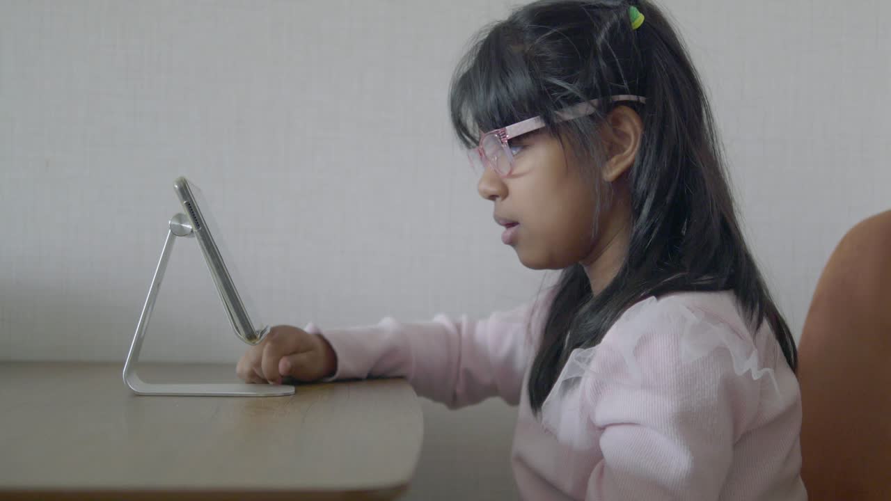 una joven sentada en un escritorio y mirando una tableta.
