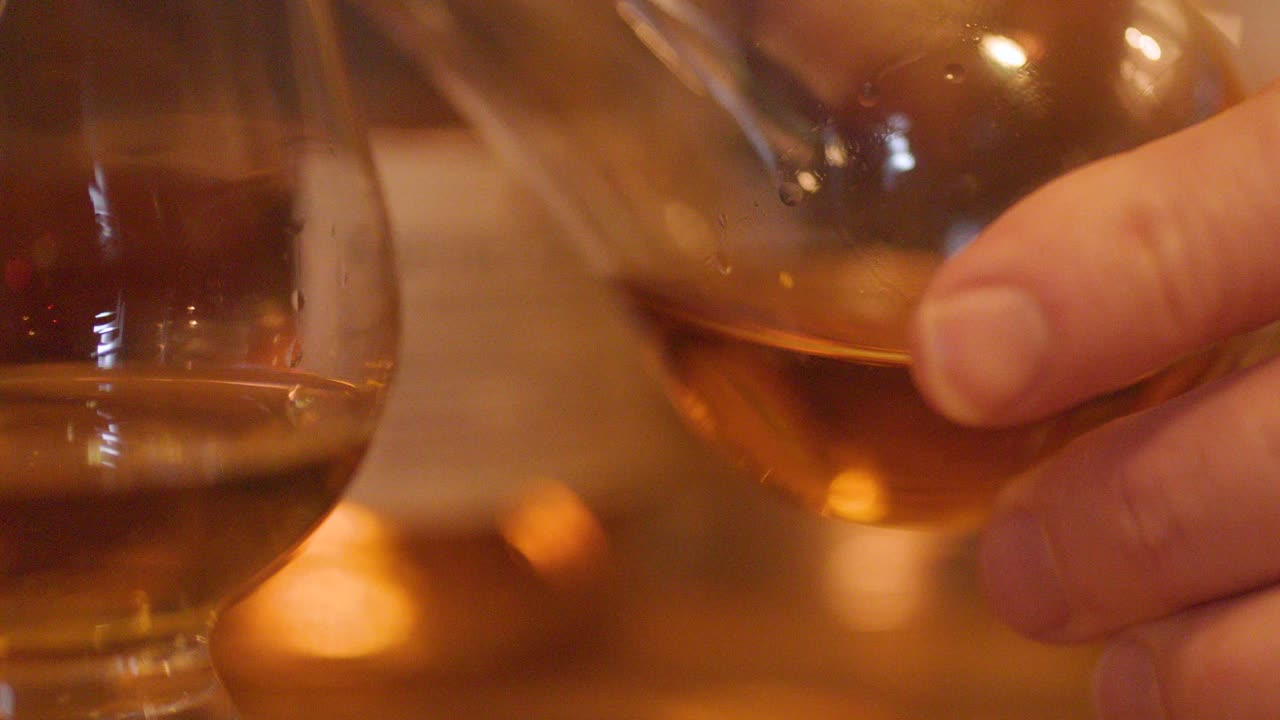 A close-up sequence shows a hand gently swirling a whisky glass on a wooden bar, with warm ambient lighting and softly blurred bottles in the background