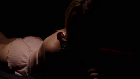 a beautiful woman lies in a dark room while she sensually plays with a red roos