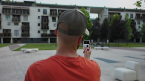 Over-The-Shoulder-View-Of-Freelancer-Holding-Insta360-Go-3-Action-Pod-In-Selfie-Vlog-Mode-And-Talking-To-Camera