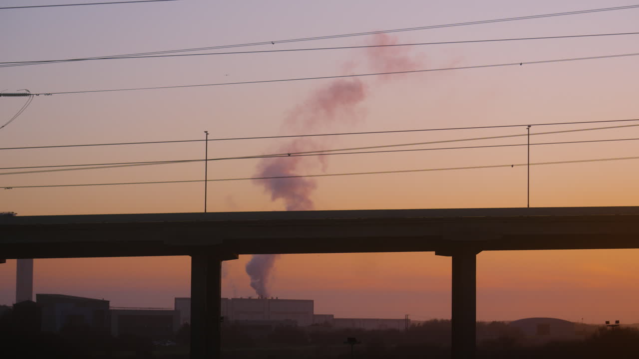 Sunset Shot of M4 Motorway Bridge with Cars Travelling Across and Factory Releasing Pollutants into Atmosphere with Pylons Carrying Electricity Energy Overhead. Transportation Footage. ProRes 4K.