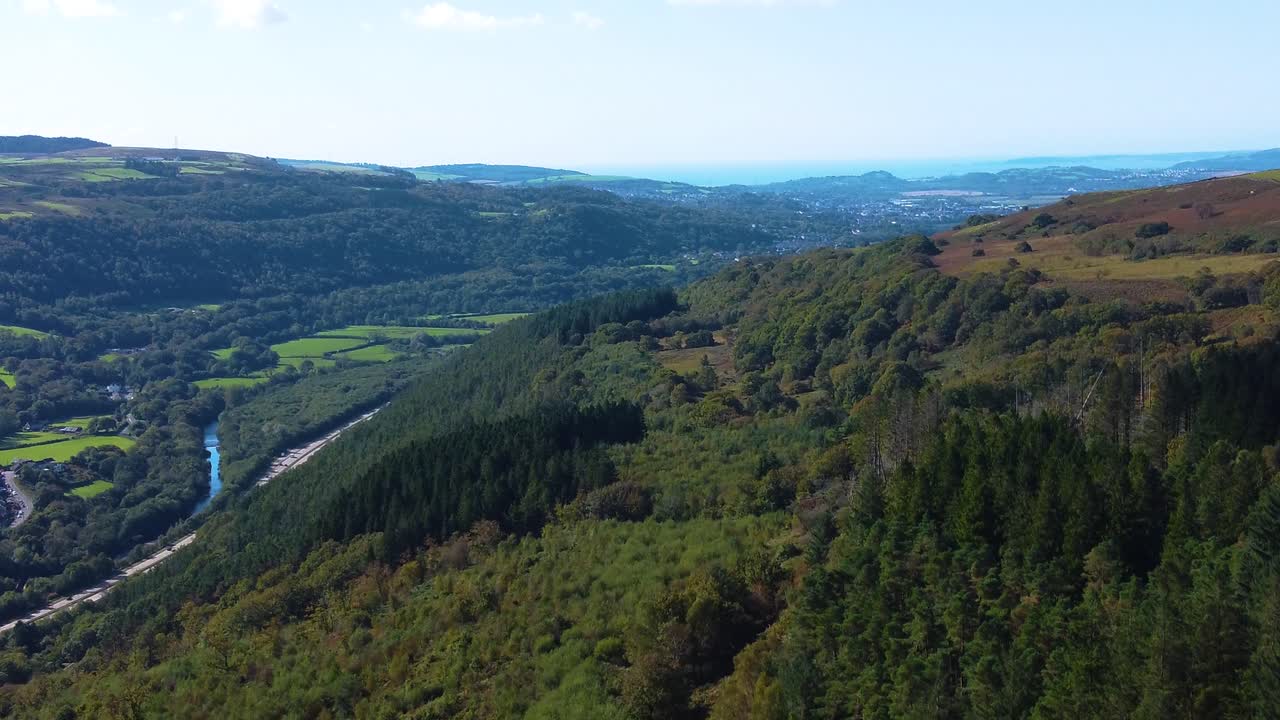 Aerial View Reaching from Deep Welsh Valley All the Way to the Ocean in Background with Winding River Neath and Dual Carriageway Road Below. Britain Viewed from the Air