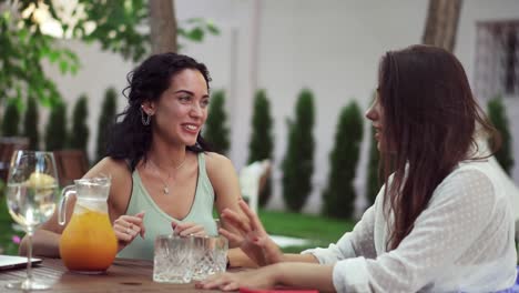 people, communication and friendship concept - two women drinking orange juice, talking at outdoor cafe, laughing